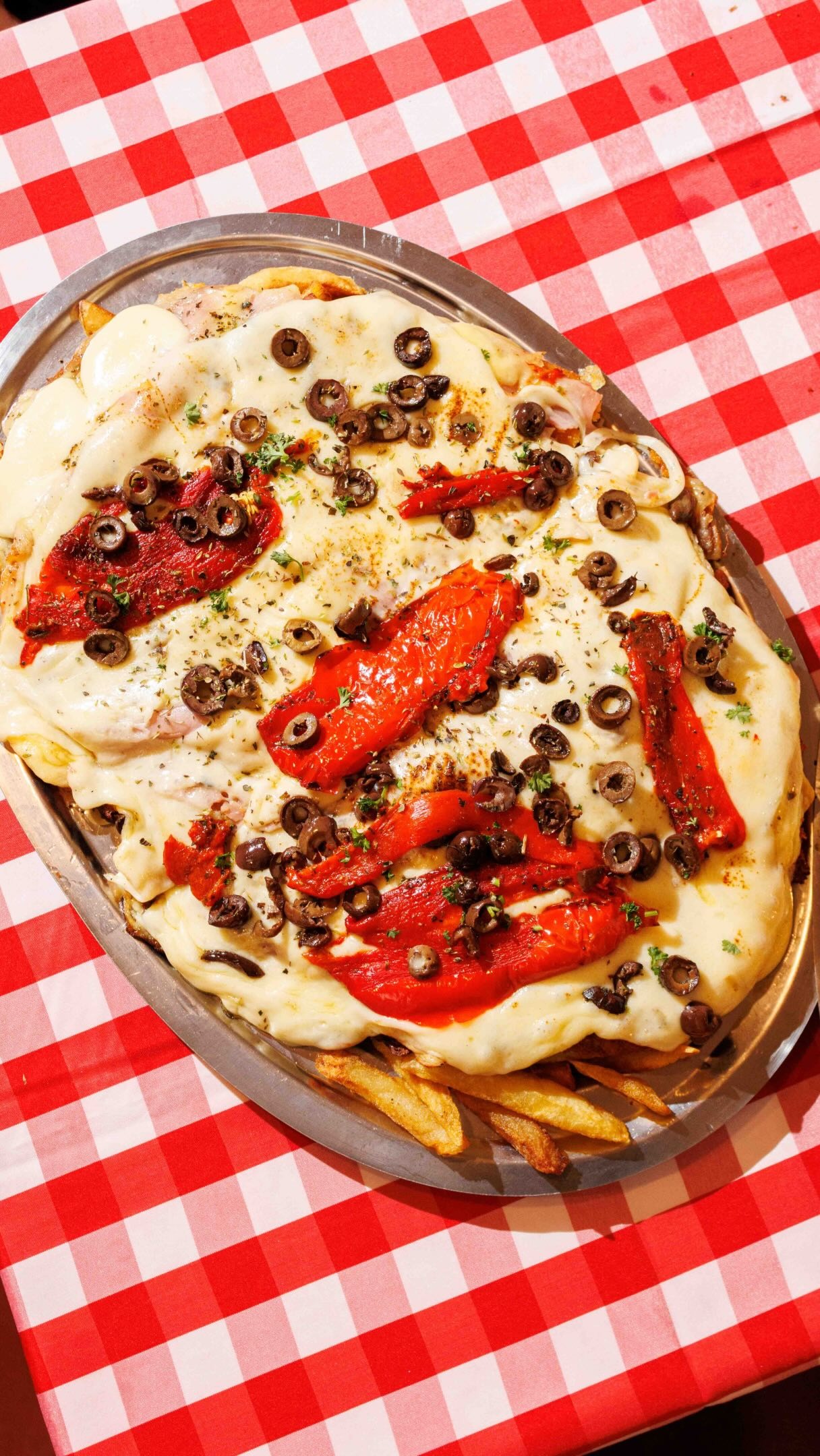 Milanesa gratinada con queso, morrones y aceitunas sobre papas fritas